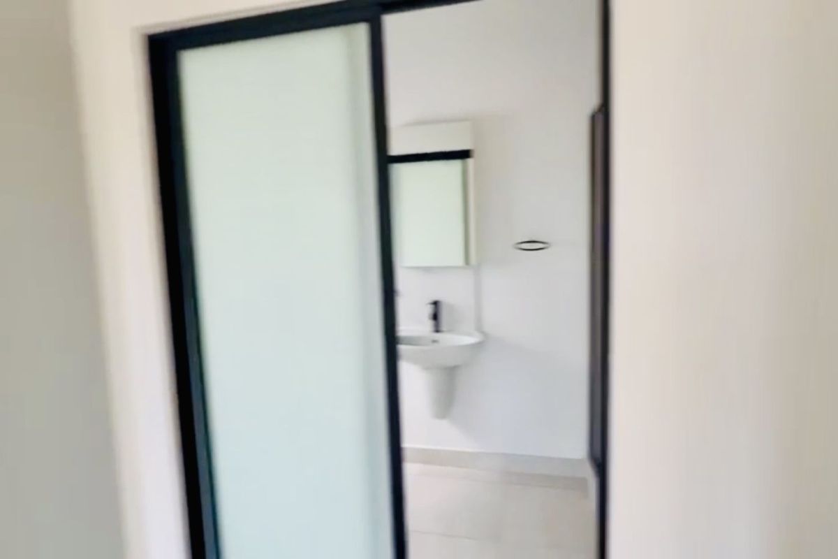 A view through a sliding door into a minimalist bathroom featuring a pedestal sink, wall-mounted mirror, and modern black fixtures.