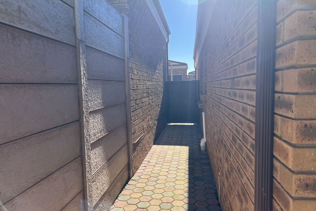 A narrow side passage featuring paved brick flooring, brick boundary walls, and a secure gate providing access to the rear of the property.