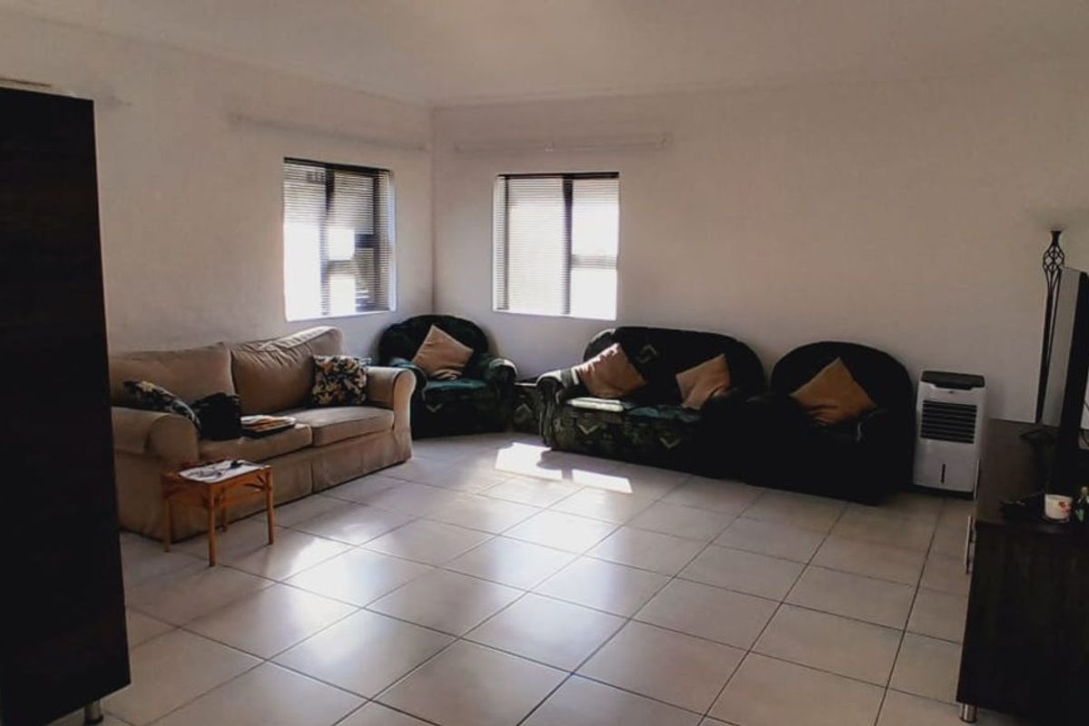 A spacious living room featuring neutral floor tiles and natural light from two windows, providing a versatile area for relaxation.