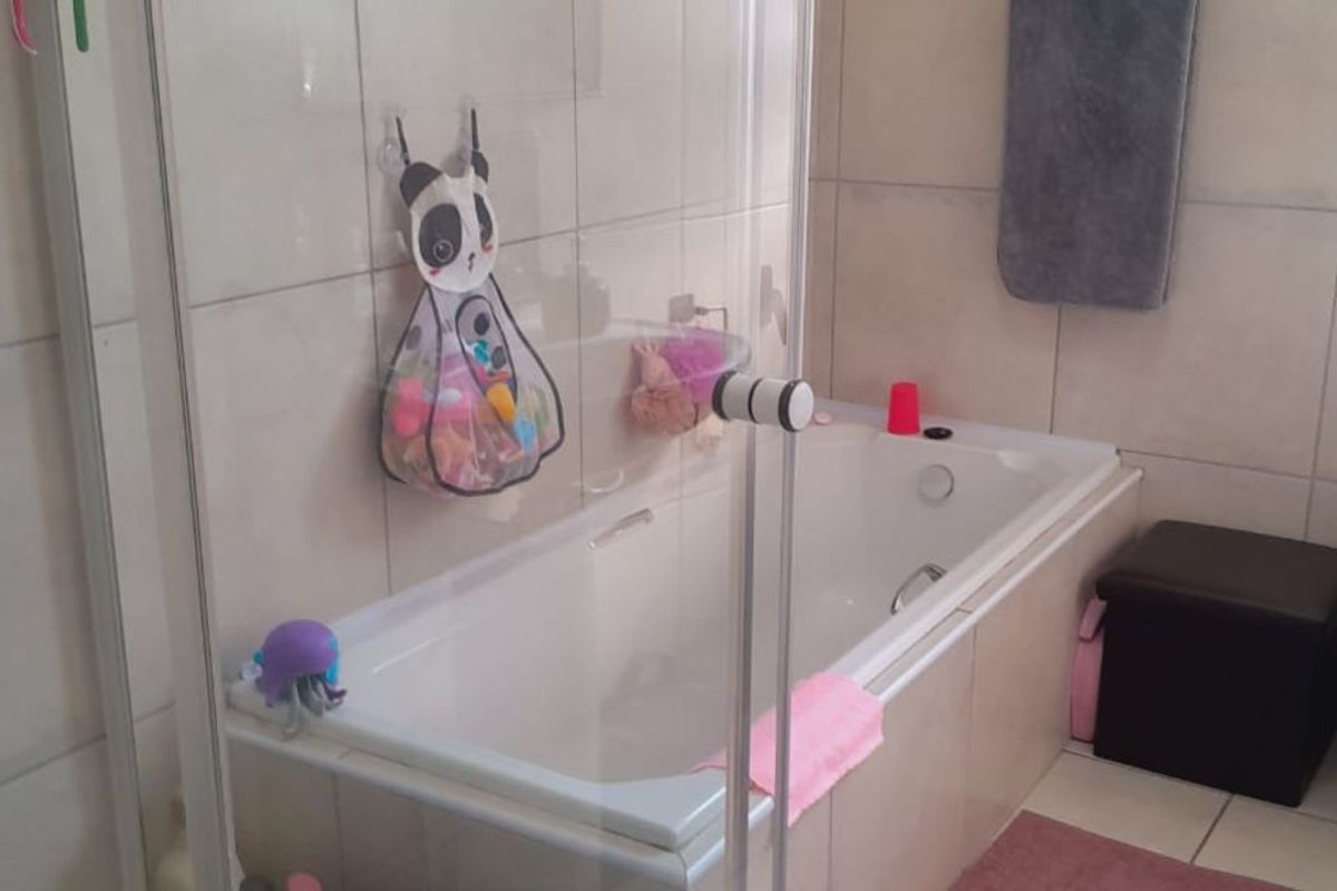 A functional bathroom featuring a built-in bathtub with glass enclosure, a standard toilet, and neutral wall tiling.