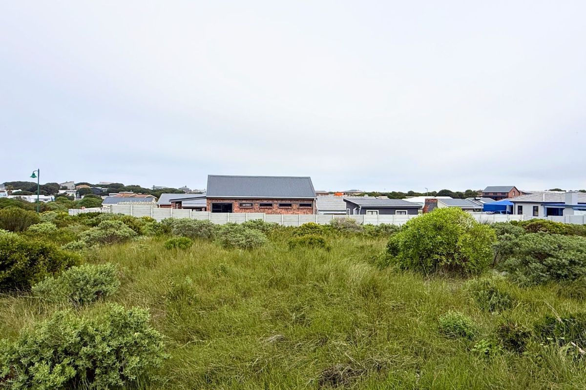 A view of a vacant residential plot featuring natural coastal vegetation, with neighboring residential properties and boundary fencing visible in the background.
