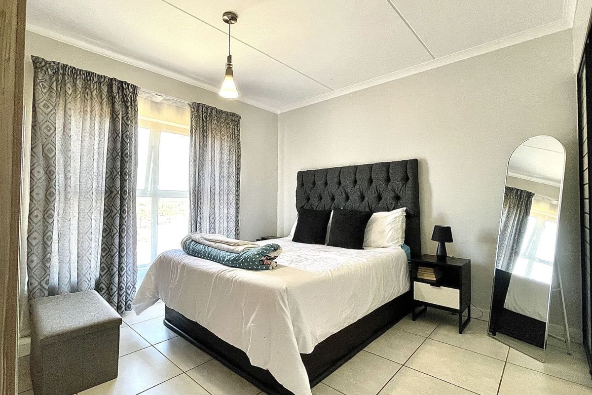 A well-lit bedroom featuring tiled flooring, a large window with curtains, and built-in cupboard space.