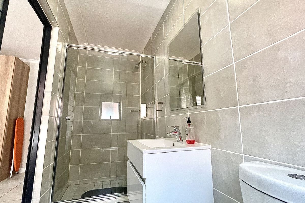 Modern bathroom featuring a glass-enclosed shower, wall-mounted vanity with integrated basin, and neutral floor-to-ceiling tiling.