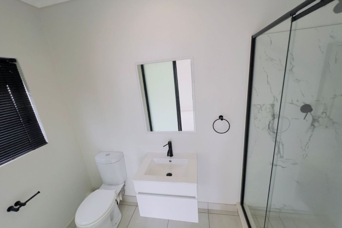 A modern bathroom featuring a wall-mounted vanity, a white toilet, and a glass-enclosed shower with marble-look wall tiles.