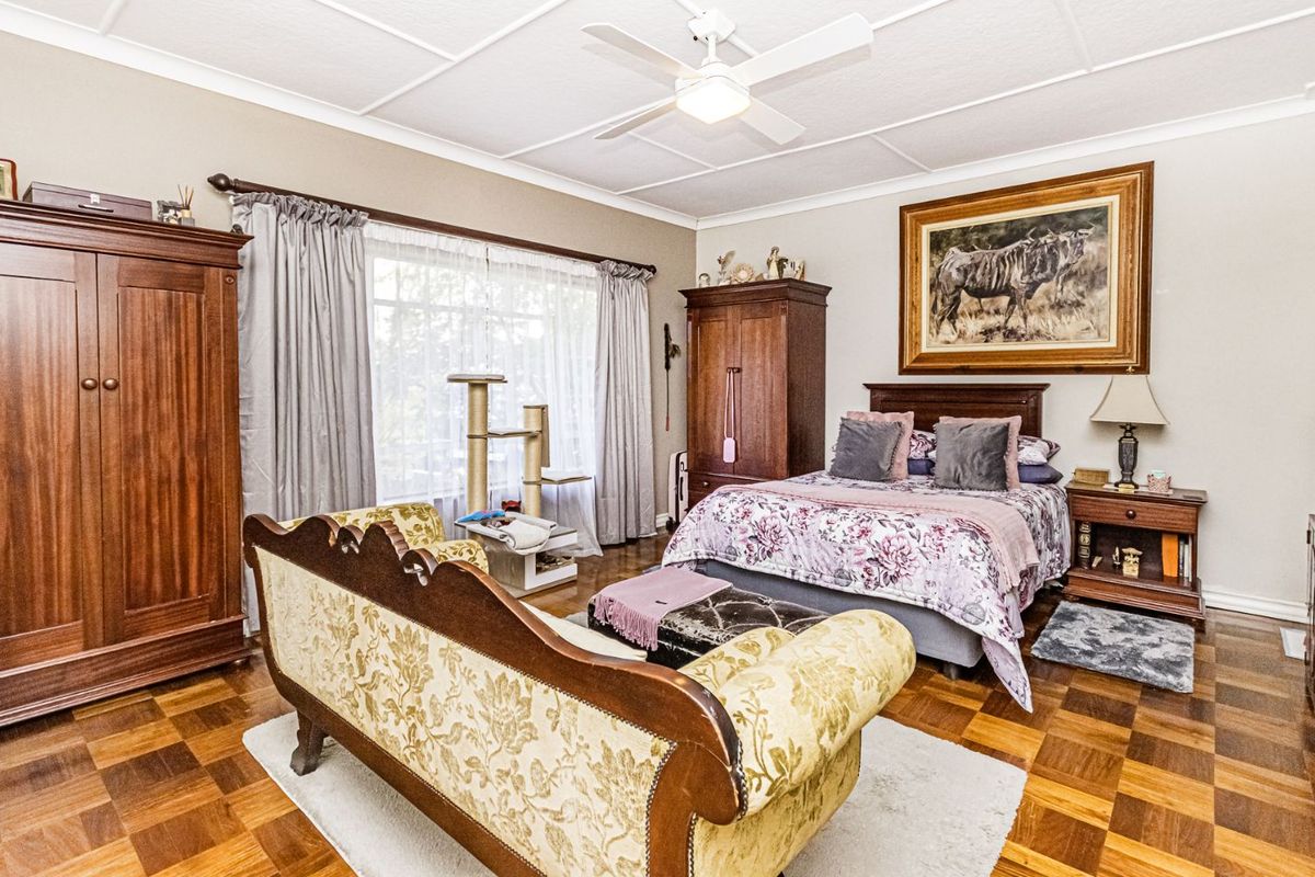 Spacious bedroom featuring classic parquet flooring, a ceiling fan, and large windows that provide ample natural light.