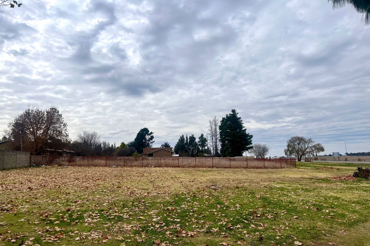 A vacant residential plot featuring open grass land and perimeter metal fencing, offering a clear space for future development.