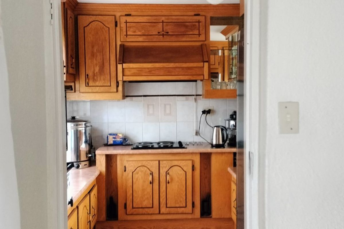 A functional kitchen featuring traditional timber cabinetry, a built-in hob, and tiled splashbacks, viewed from an adjacent room.