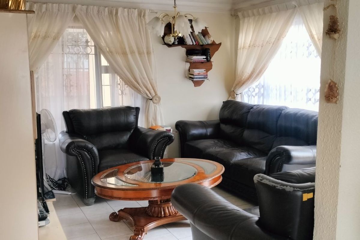 A living room area featuring tiled flooring, large windows with curtains, and a central ceiling light fixture.