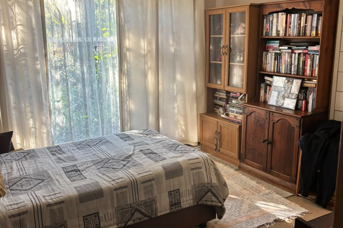 A bedroom featuring classic cornice detailing and a large window with security gate, providing natural light and a view of the garden.