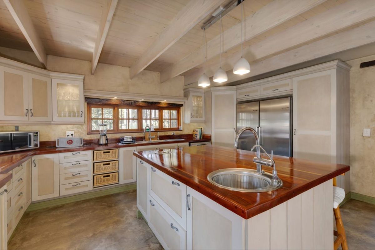 Spacious kitchen featuring a large wooden island with a prep sink, custom cabinetry, stainless steel refrigerator, and exposed timber beam ceiling.