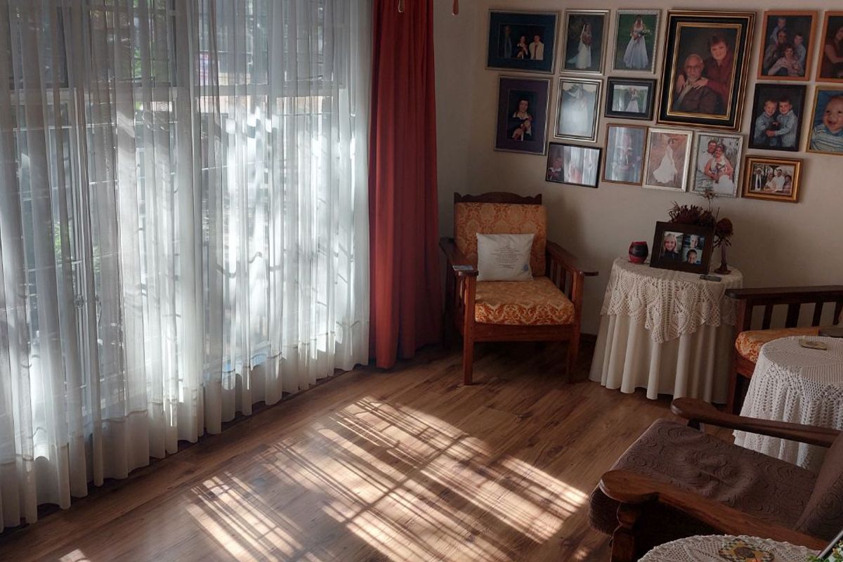 A bright living room featuring wood-look flooring and large floor-to-ceiling windows with sheer curtains, creating a warm and inviting atmosphere.