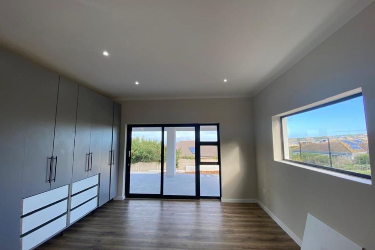 A bright, modern room featuring built-in grey cabinetry, wood-look flooring, recessed lighting, and large sliding glass doors leading to an outdoor patio area.