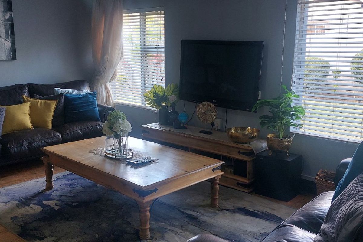 A comfortable living room featuring timber flooring, dual windows with fitted blinds, and a wall-mounted television setup.
