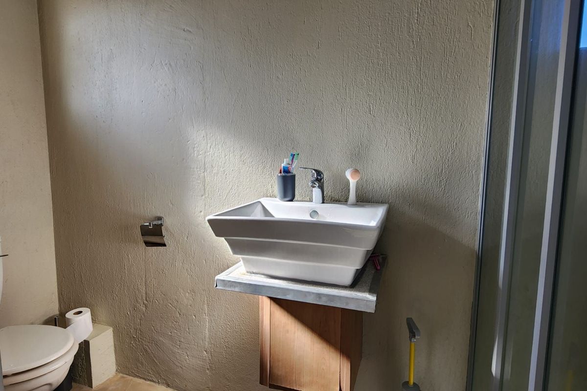 A functional bathroom featuring a wall-mounted vessel sink, a toilet, and a shower enclosure with textured wall finishes.