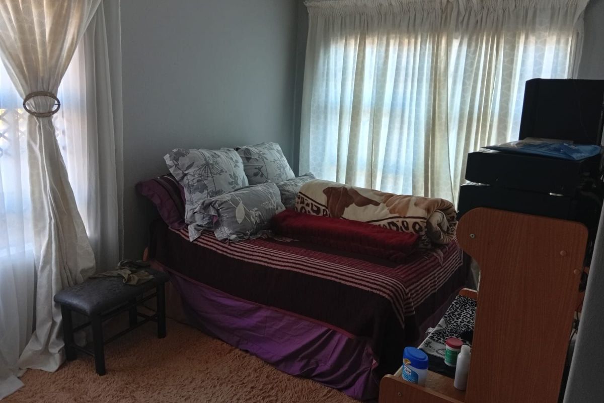 A bedroom featuring natural light through large windows, neutral wall tones, and carpeted flooring.