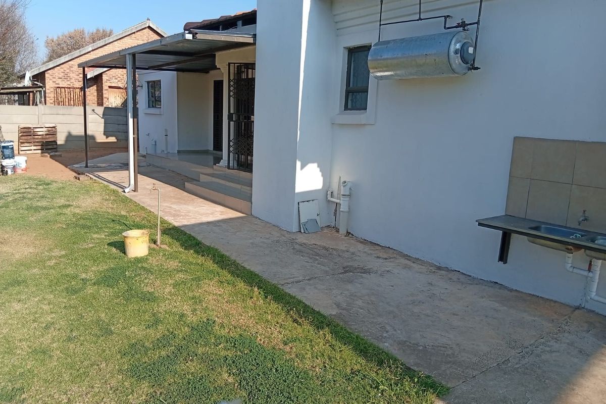 Rear exterior view of the house featuring a paved patio area, an outdoor sink station, and an external geyser unit.
