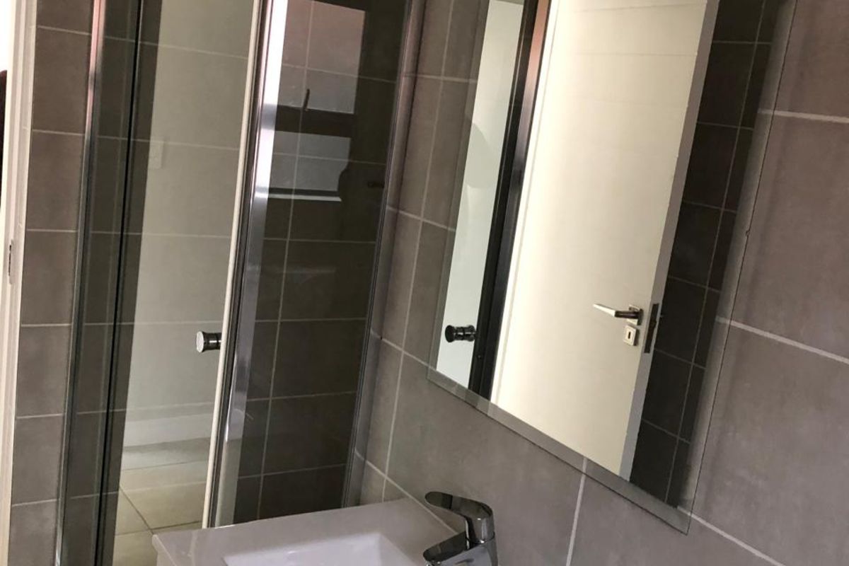 Modern bathroom featuring a glass-enclosed shower, a wall-mounted vanity with a basin, and neutral wall tiling.