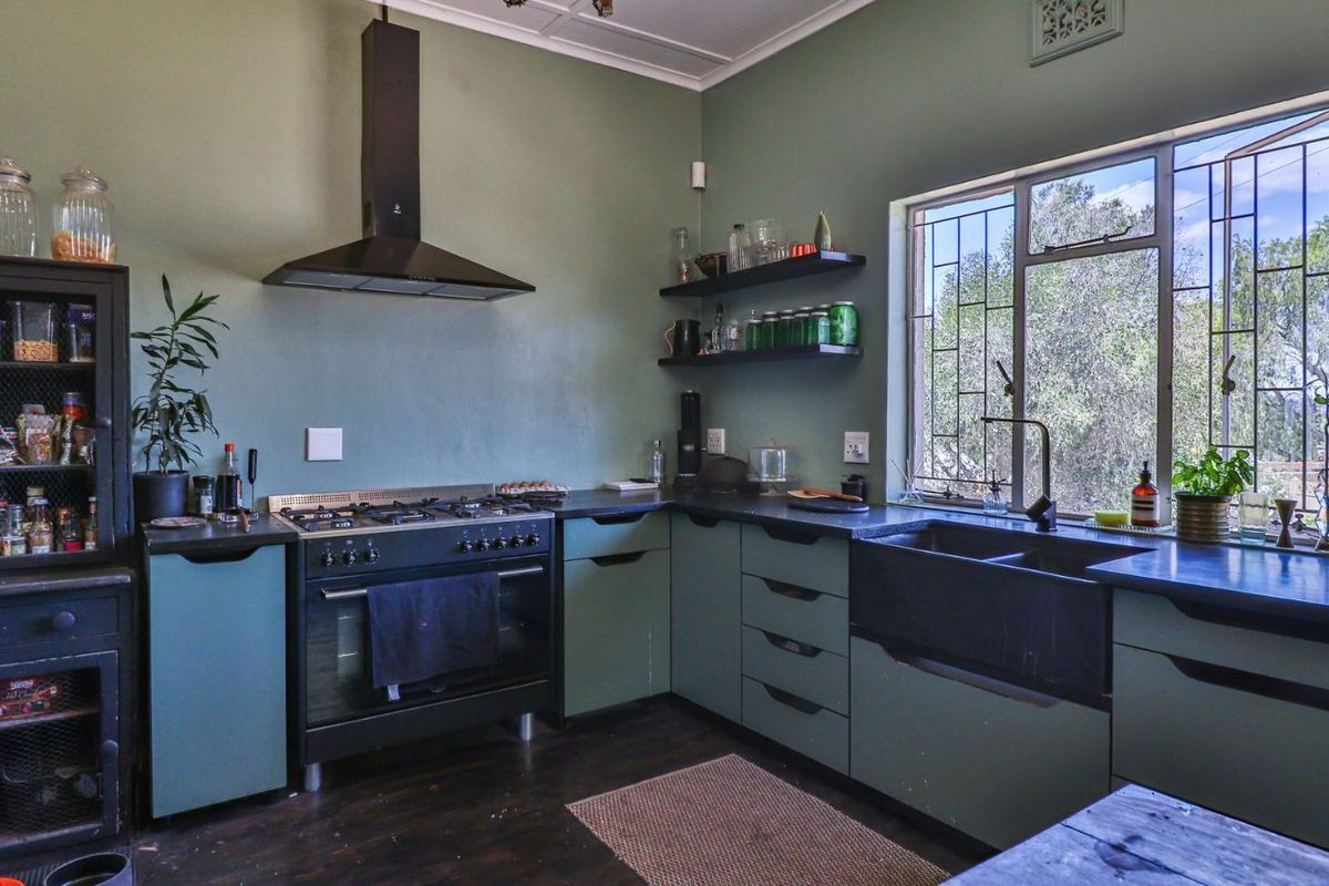 A well-appointed kitchen featuring sage green cabinetry, a black farmhouse sink, a gas stove with an extractor fan, and dark countertops.