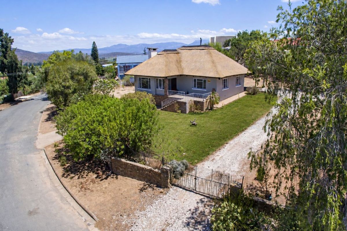 Aerial view of a detached house featuring a traditional thatched roof, front porch, and a spacious garden with a gravel driveway.