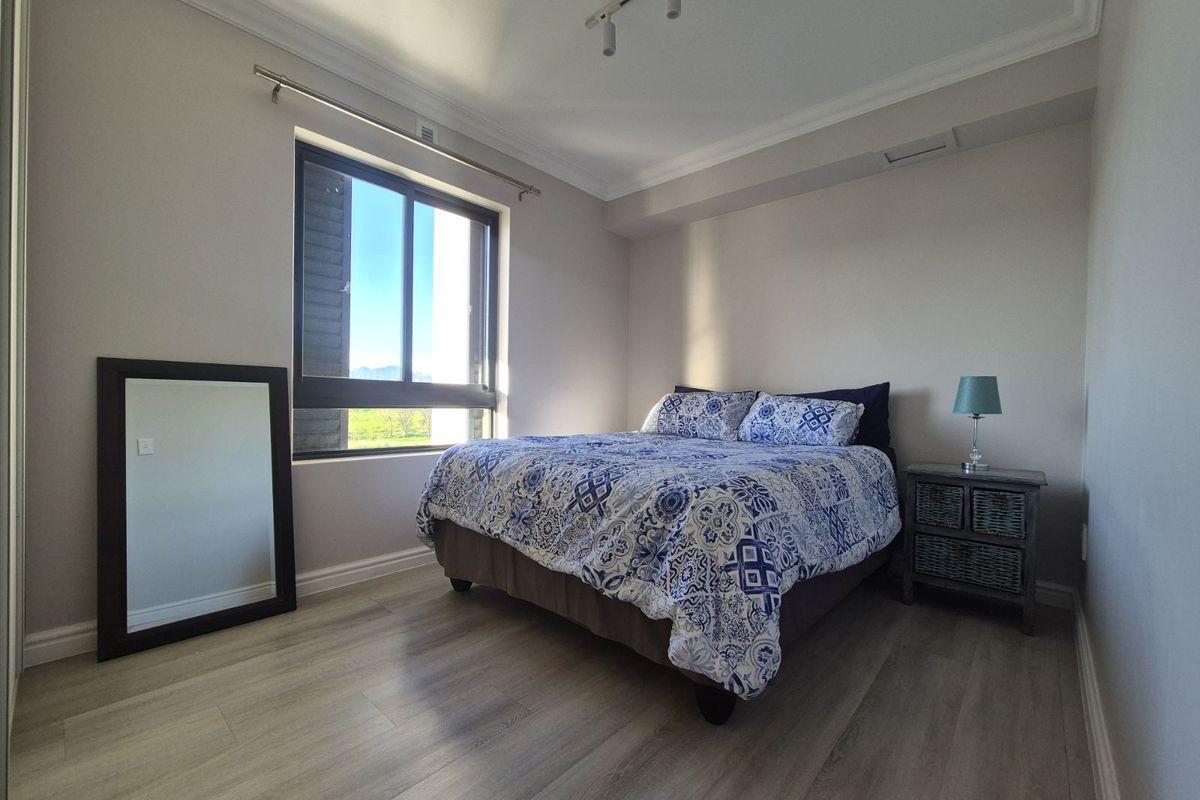 A well-maintained bedroom featuring light wood-look flooring, crown molding, and a large window providing natural light and exterior views.