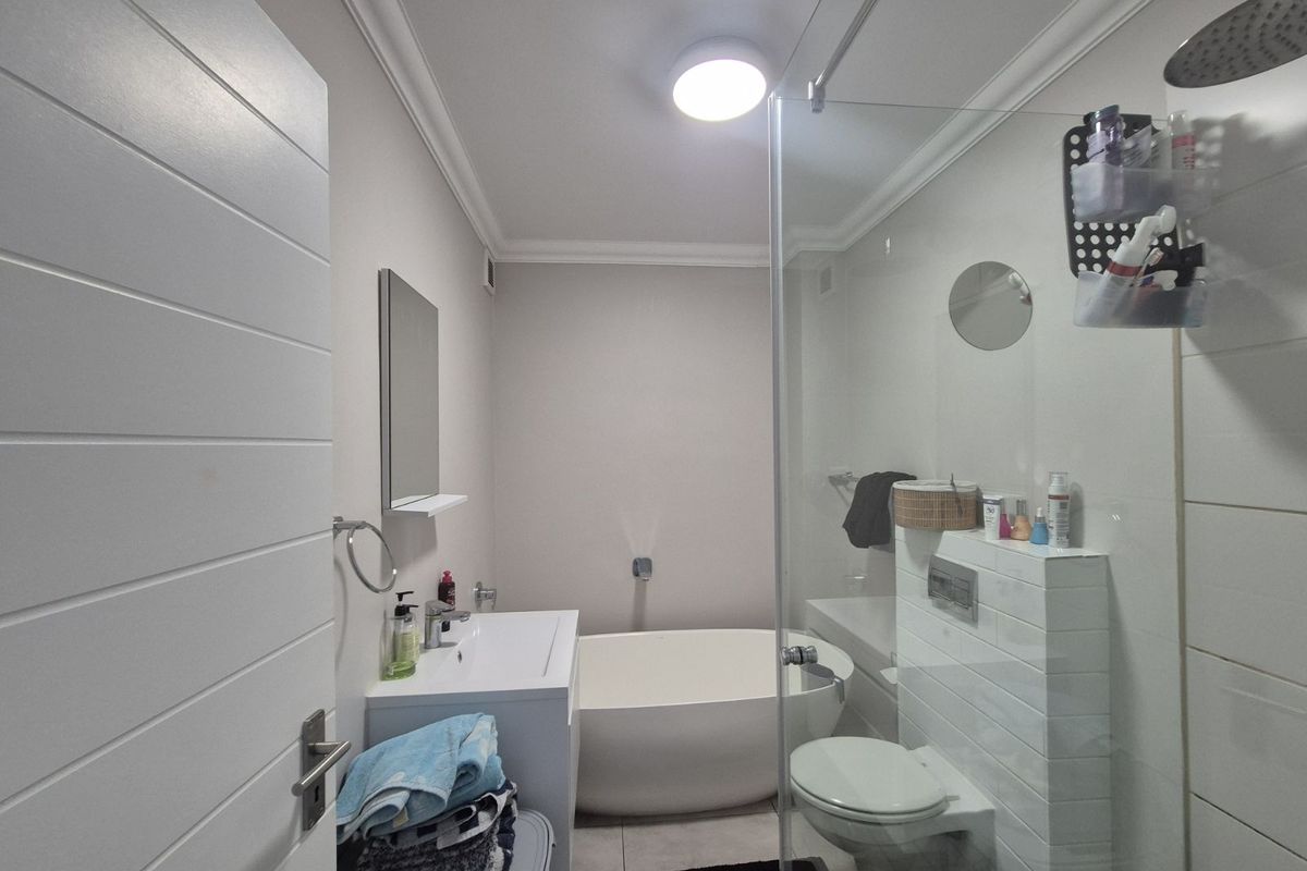 Modern bathroom featuring a freestanding bathtub, wall-mounted toilet with concealed cistern, glass shower enclosure with rainfall showerhead, and a vanity basin.
