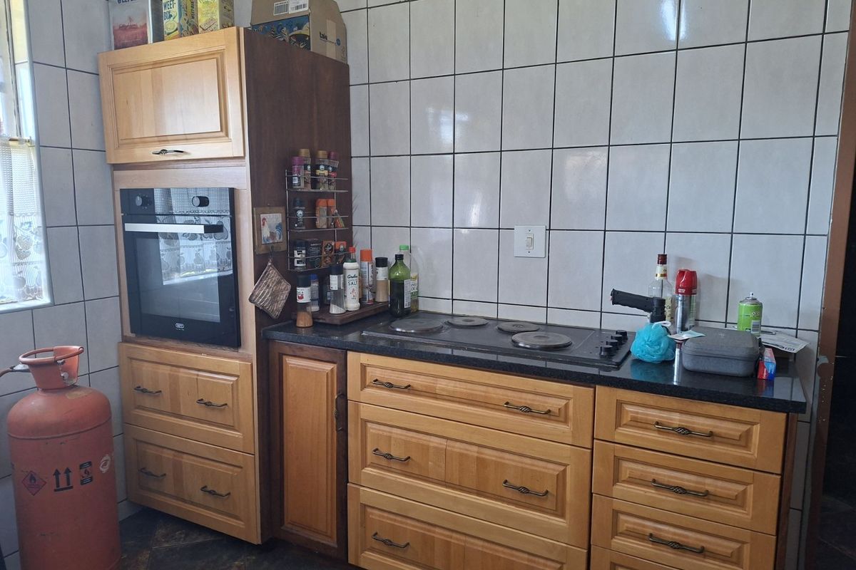 A functional kitchen area featuring built-in wooden cabinetry, a wall-mounted oven, and a solid surface countertop with an integrated electric hob.