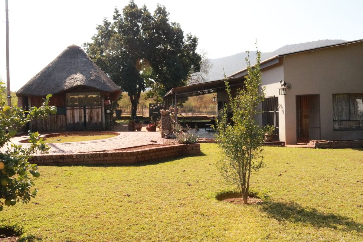 A spacious farm garden featuring a traditional thatched lapa, brick-paved patio area, and established lawn with mountain views in the background.
