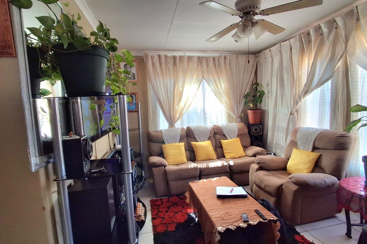 A cozy living room featuring a ceiling fan, tiled flooring, and large windows dressed with curtains, providing a comfortable and functional living space.