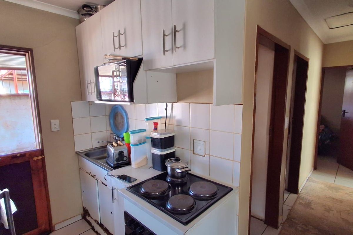Compact kitchen featuring white cabinetry, a built-in electric hob, and tiled splashbacks, with direct access to an adjacent hallway.