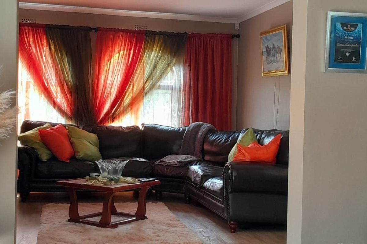 A comfortable living room featuring laminate flooring, neutral wall tones, and large windows dressed with layered curtains.