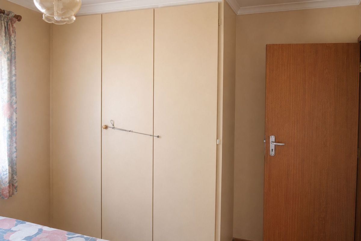 A bedroom featuring built-in floor-to-ceiling cabinetry, crown molding, and a wooden interior door.