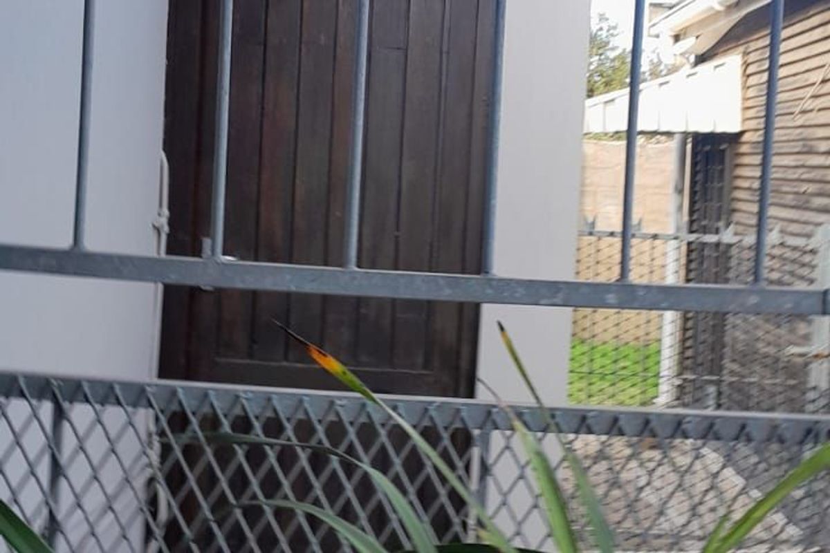 A view of a side exterior area featuring a wooden door and metal security fencing.