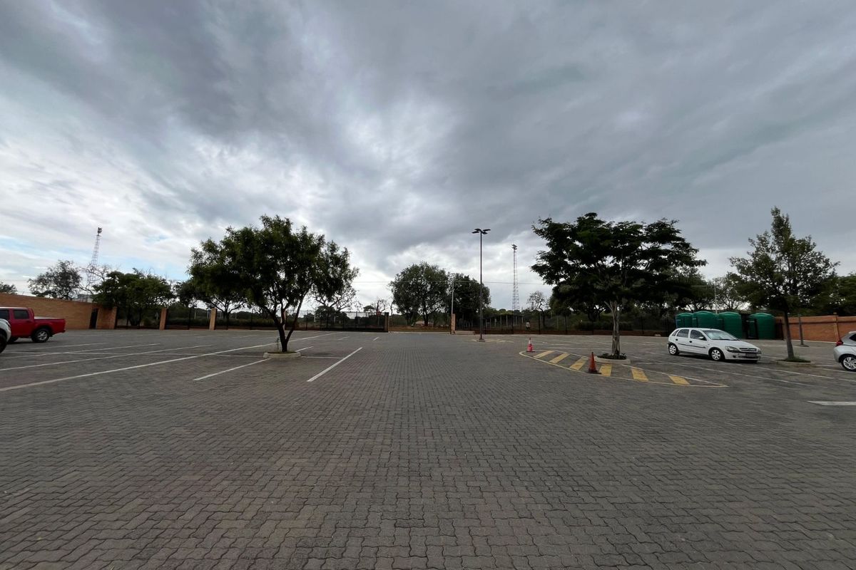 A paved outdoor parking area featuring marked bays, mature trees, and perimeter fencing.