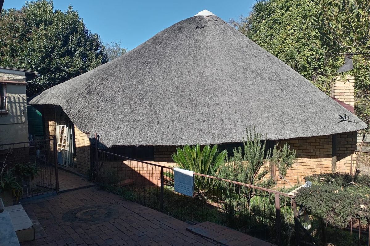 Exterior view of a traditional thatched-roof dwelling featuring brick construction and a paved courtyard area.