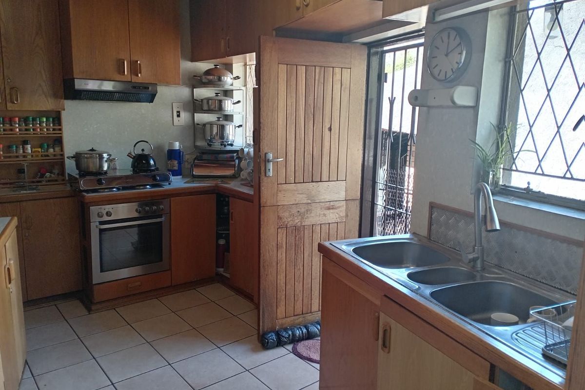 A functional kitchen featuring wooden cabinetry, a built-in oven with extractor fan, double sink, and tiled flooring with direct access to the exterior.