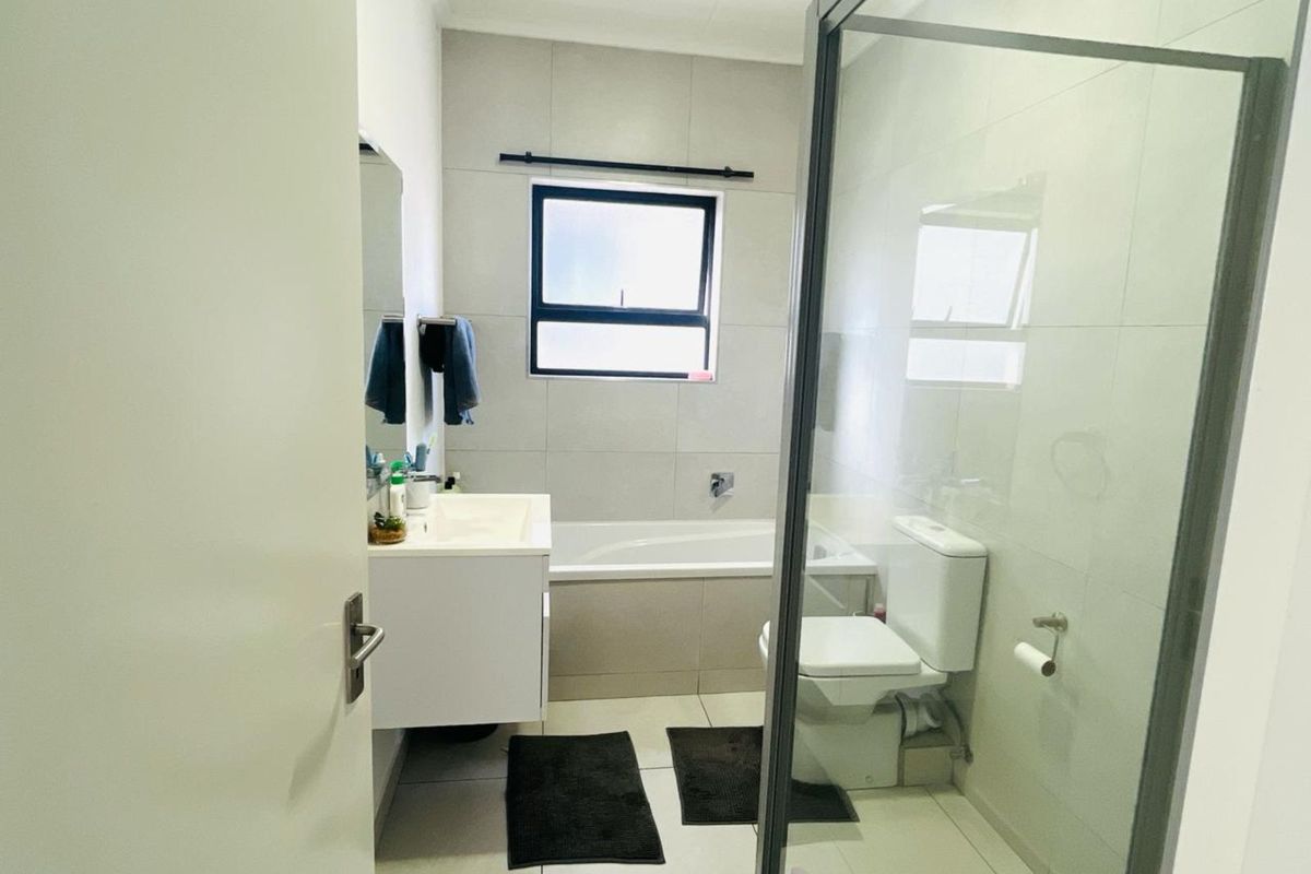 Modern bathroom featuring a built-in bathtub, glass-enclosed shower, wall-mounted vanity, and neutral floor-to-ceiling tiling.