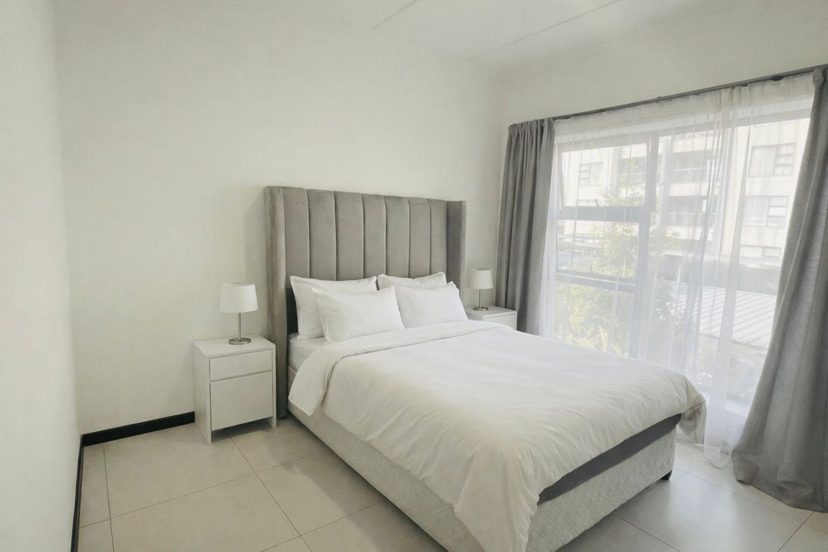 A bright and modern bedroom featuring neutral tiled flooring, large windows with curtain tracks, and a clean, minimalist aesthetic.