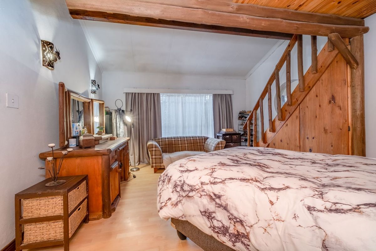 A bedroom featuring exposed timber ceiling beams and a wooden staircase leading to an upper level, with light wood-look flooring.