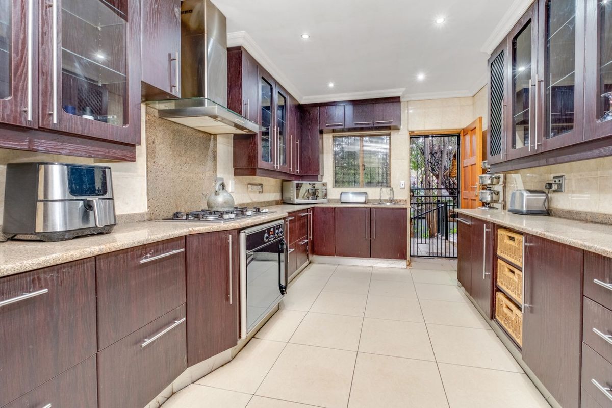 A well-appointed kitchen featuring dark wood cabinetry, granite countertops, a built-in gas hob, stainless steel extractor fan, and tiled flooring with direct outdoor access.