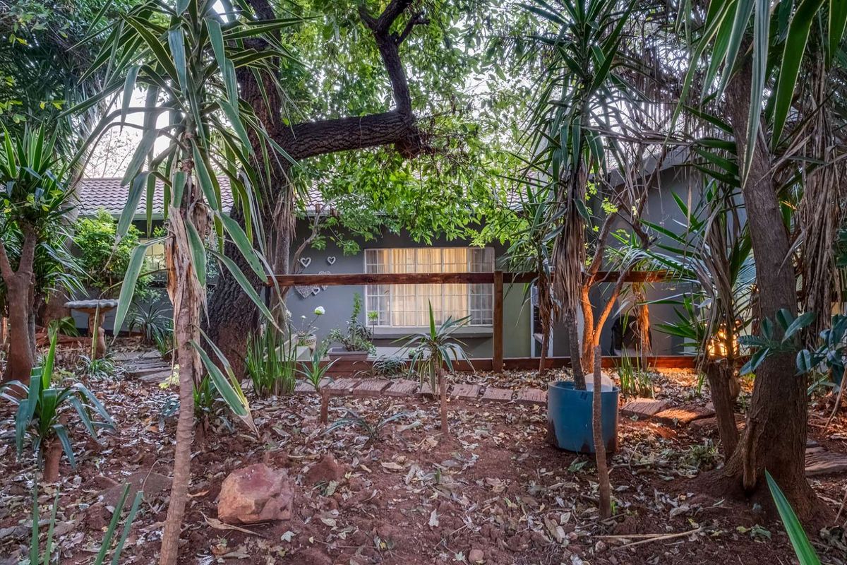 A view of the rear exterior of the house, featuring a garden area with mature trees, established landscaping, and a wooden fence.