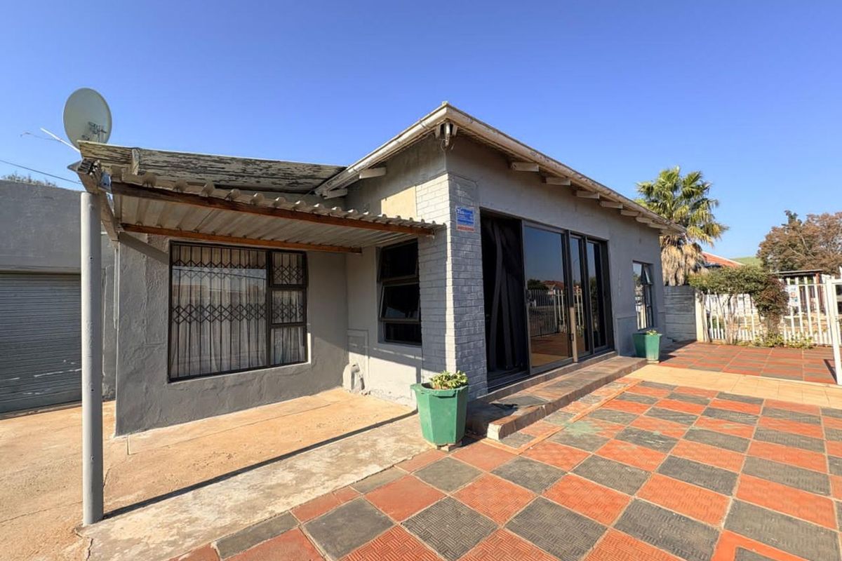 Exterior view of the house featuring a paved patio area, sliding glass doors, security gates, and a covered side walkway.