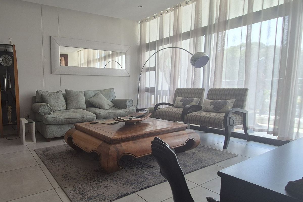 A bright and spacious living room featuring large floor-to-ceiling windows with sheer curtains, tiled flooring, and recessed ceiling lighting.
