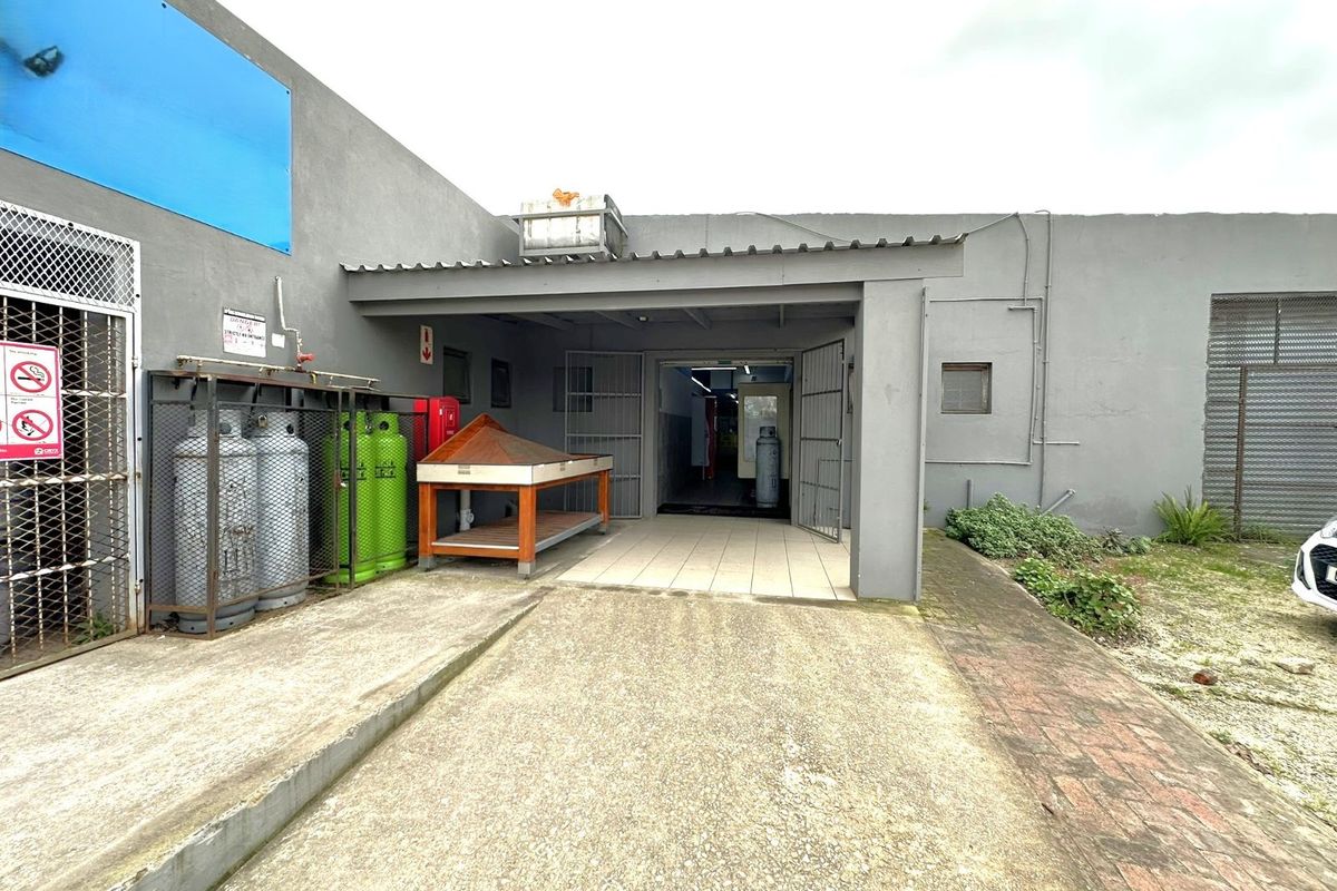 Exterior view of a commercial property entrance featuring a covered patio area, tiled flooring, and secure metal gate access.