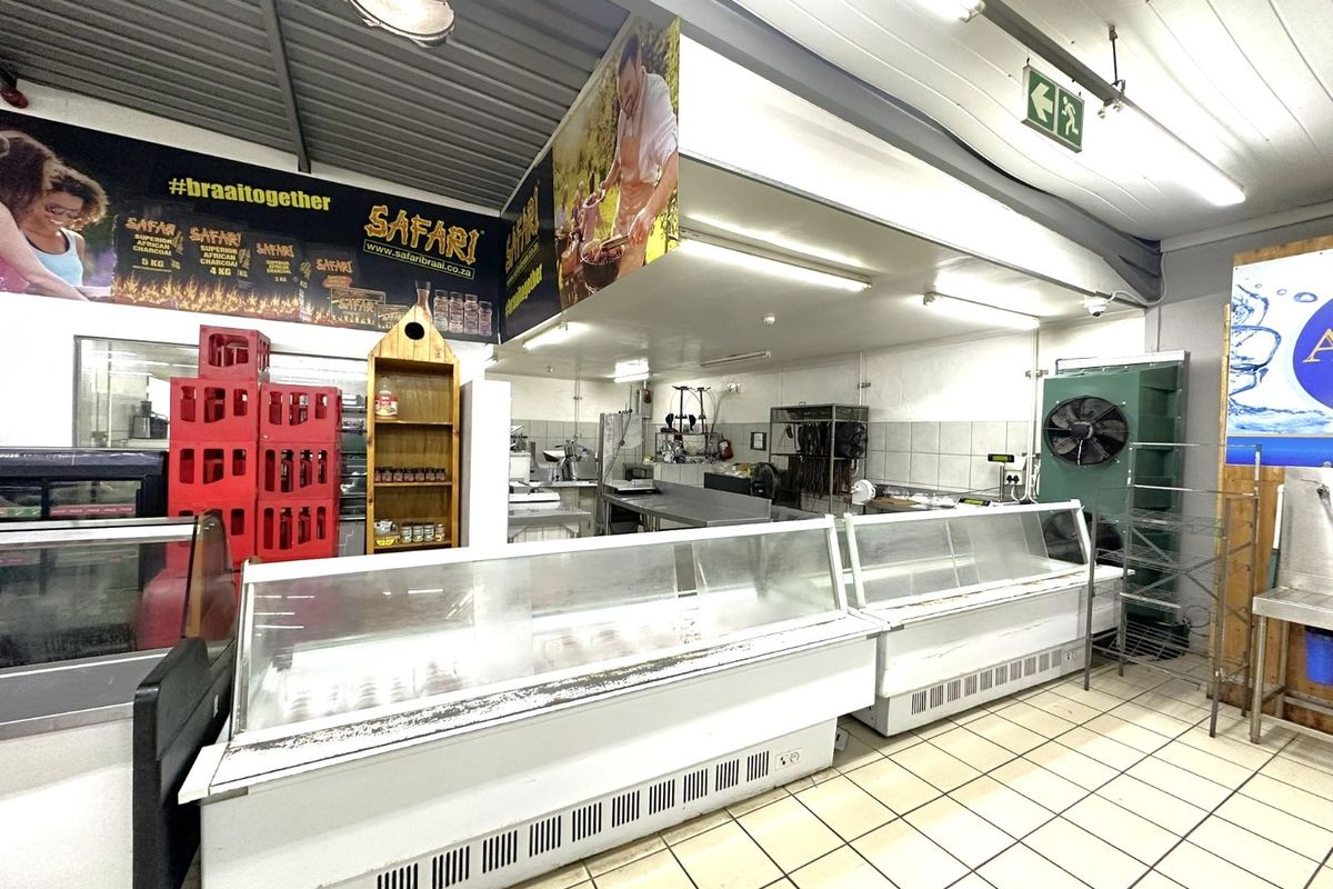 A functional retail butchery space featuring commercial refrigerated display counters, tiled flooring, and industrial lighting fixtures.