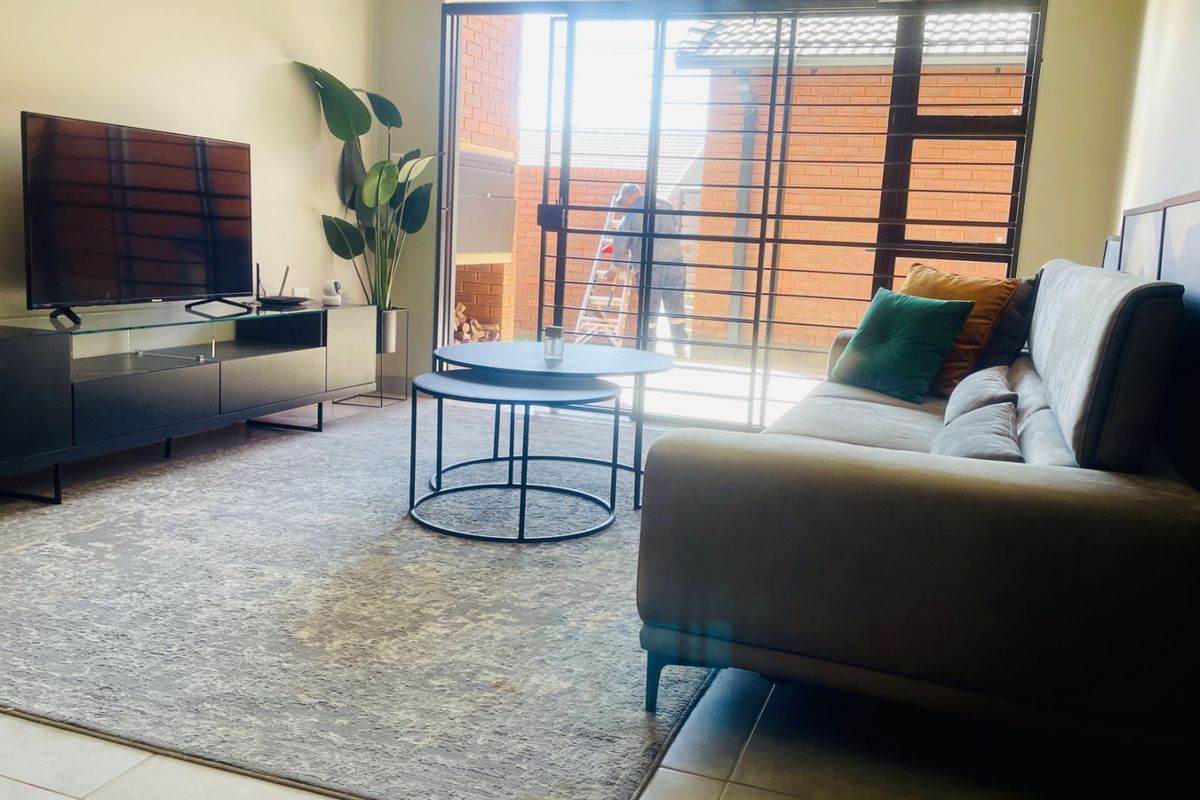A bright living room featuring large sliding glass doors that open onto a private patio area with a built-in braai.