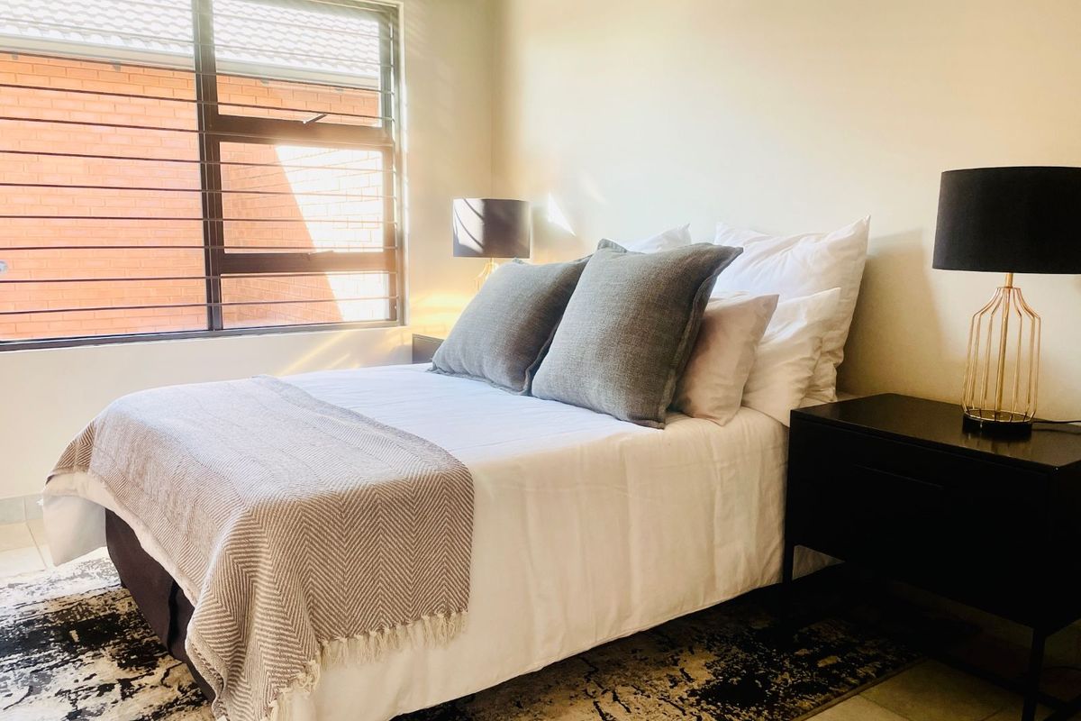 A well-lit bedroom featuring neutral wall finishes, tiled flooring, and a large window with security bars.
