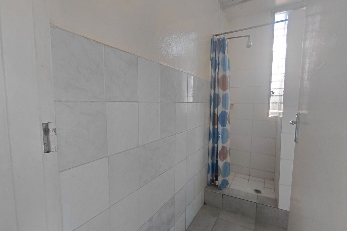 A functional bathroom featuring a walk-in shower area with tiled walls and flooring, requiring cosmetic updates to improve the overall finish.