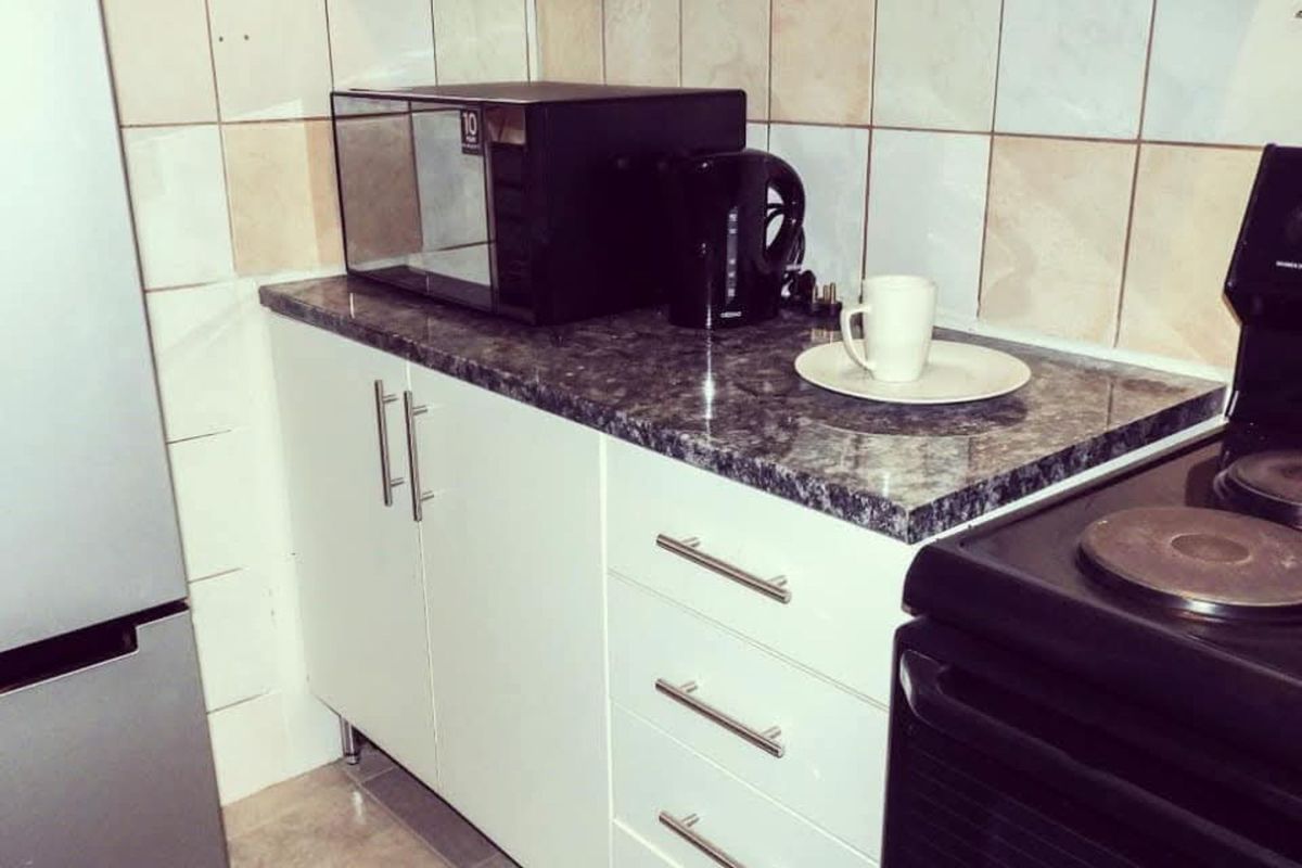 A compact kitchen area featuring white cabinetry, dark laminate countertops, and tiled splashbacks, providing a functional workspace for daily meal preparation.