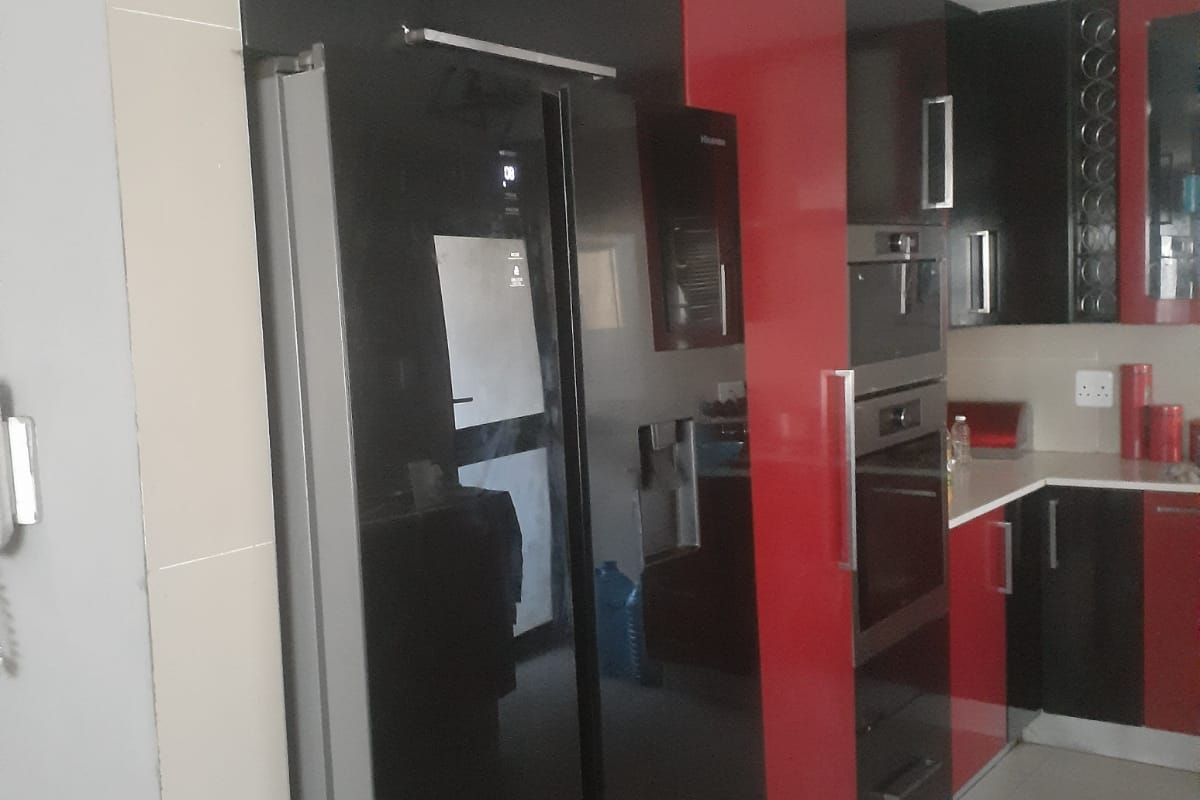 Modern kitchen featuring high-gloss black and red cabinetry, integrated oven, and built-in microwave with tiled flooring.