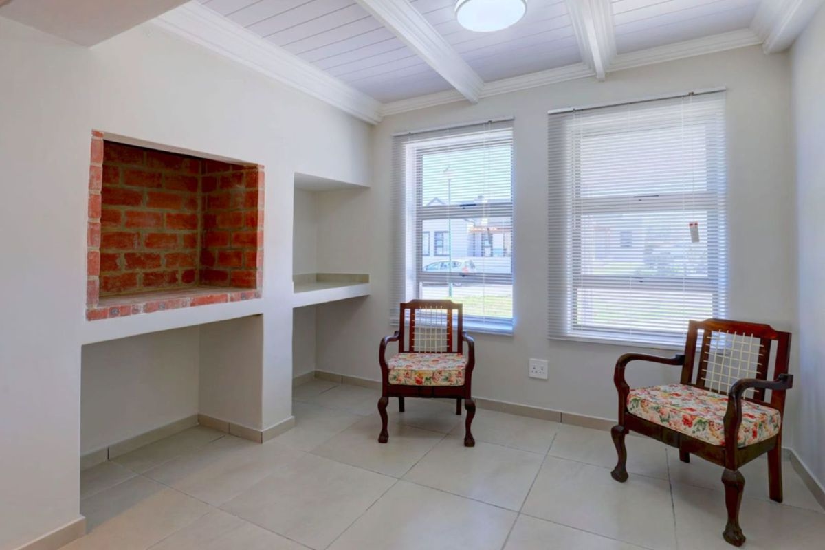 A bright living area featuring a built-in brick fireplace, tiled flooring, and large windows with fitted blinds, offering a clean and neutral space.